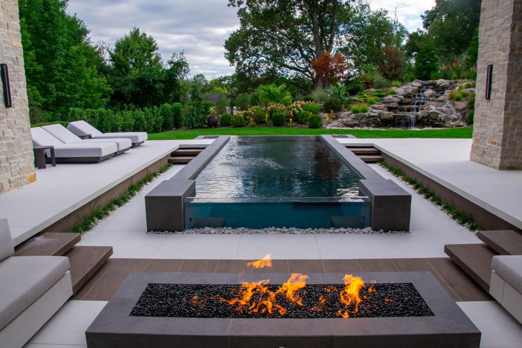 modern backyard design with glass wall pool and a sunken fire pit seating area